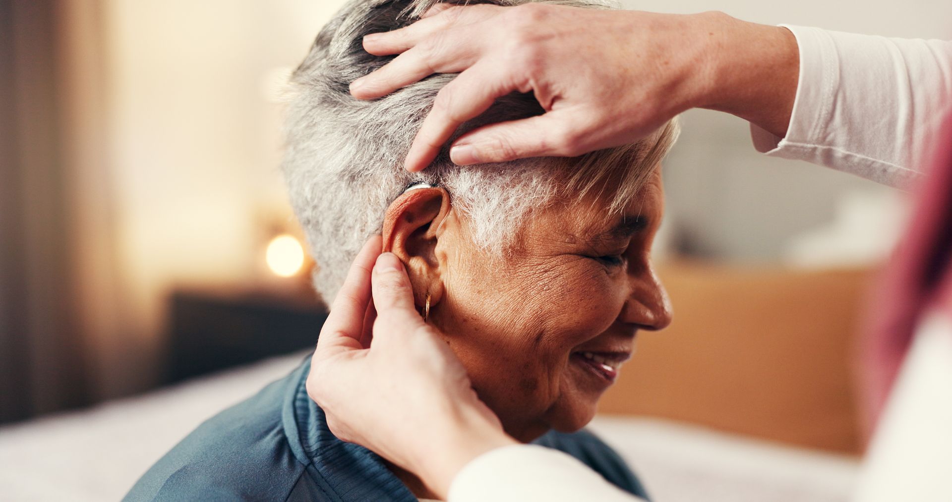 Des mains ajustent délicatement l'oreille d'une personne âgée dans un intérieur à l'éclairage tamisé.