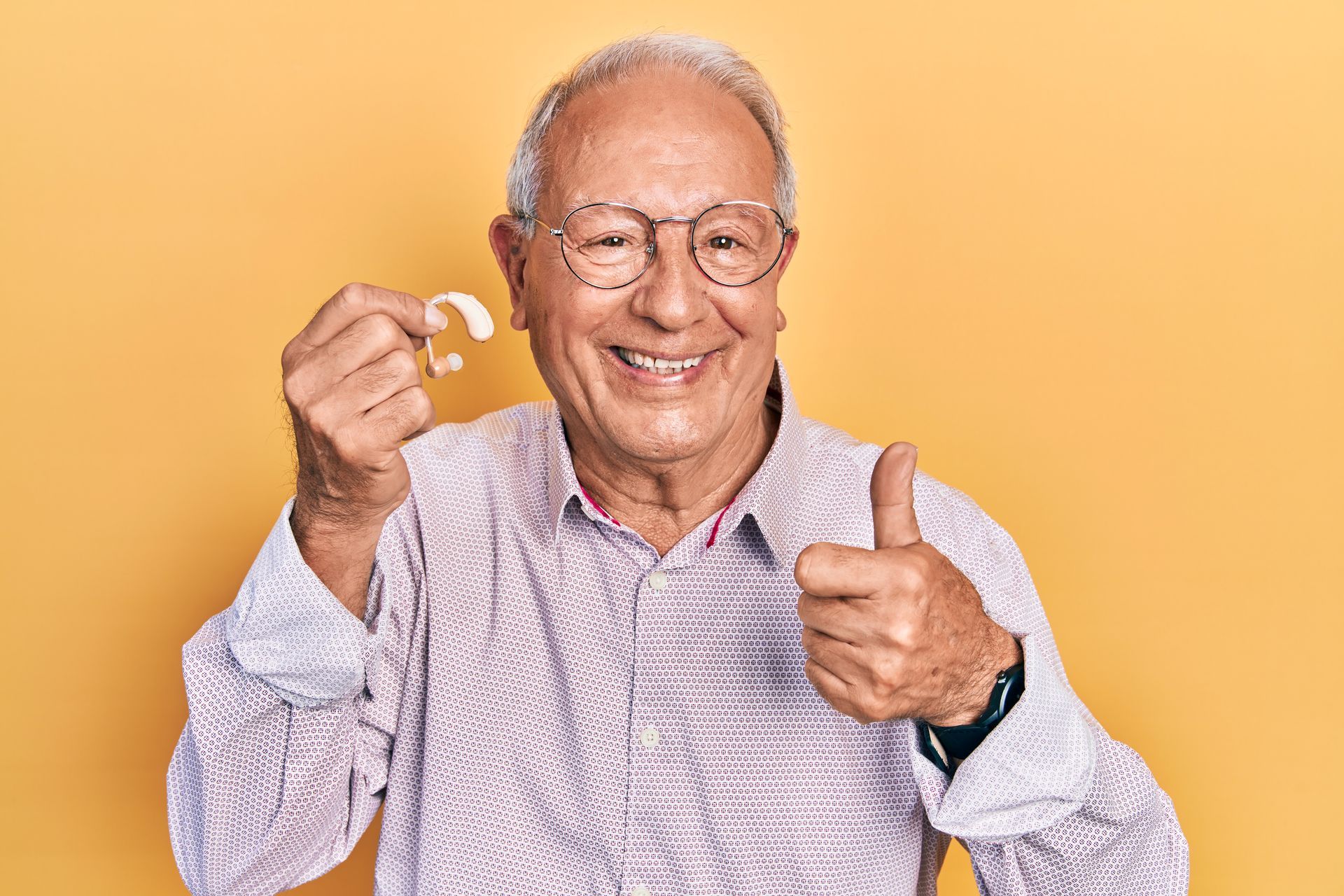 Un homme souriant portant des lunettes fait un signe de pouce levé et tient un petit objet.