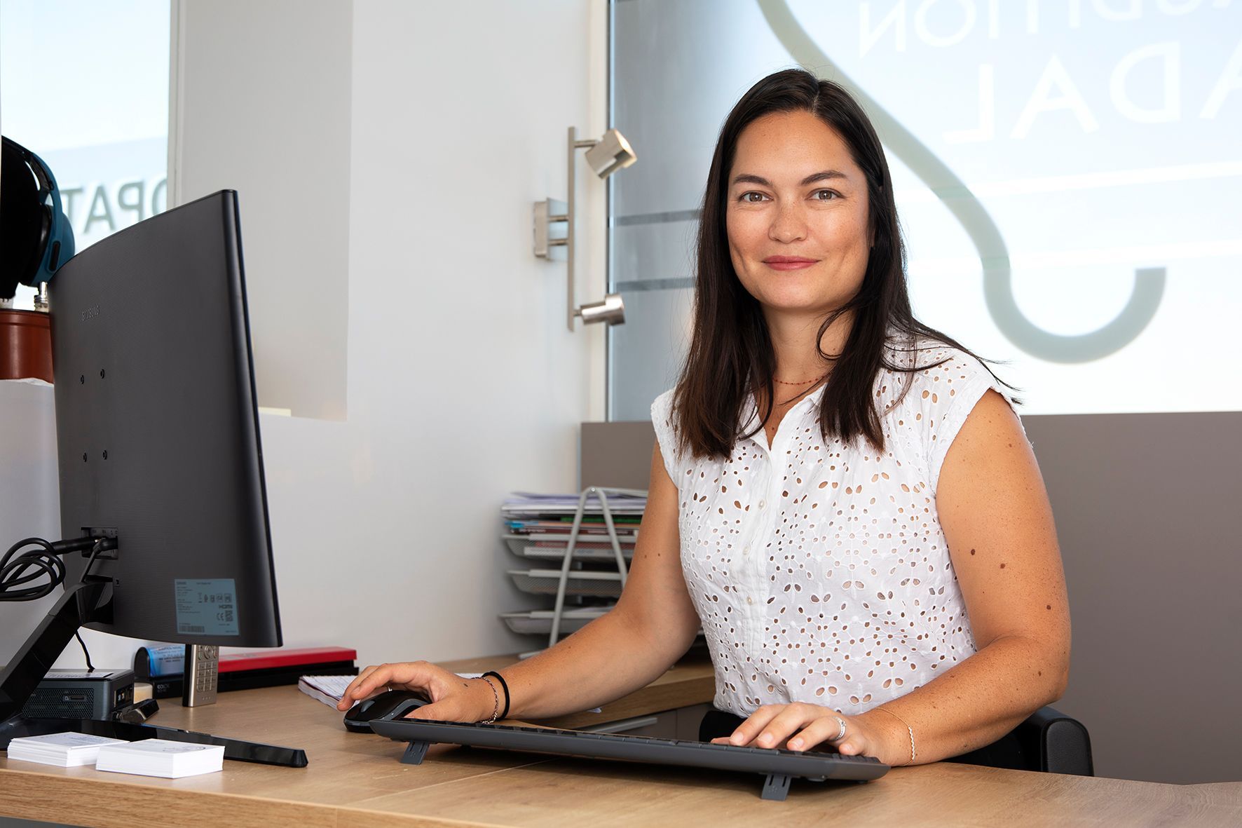 Femme assise à un bureau utilisant un ordinateur dans un environnement de bureau.