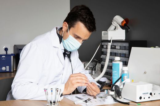 Un scientifique en blouse et masque manipule des échantillons sur une paillasse de laboratoire.
