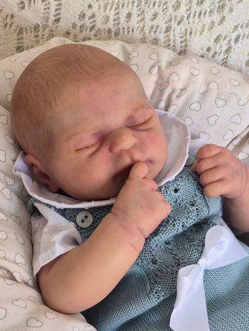 Bebé durmiendo con los ojos cerrados, descansando sobre una suave manta con un conjunto azul.
