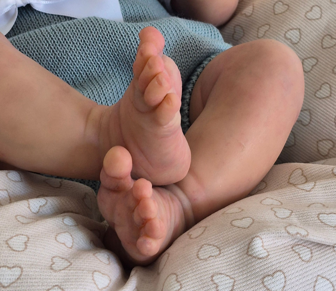 Pies de bebé descansando sobre una manta blanca, con la mano de un adulto tocándolos suavemente.