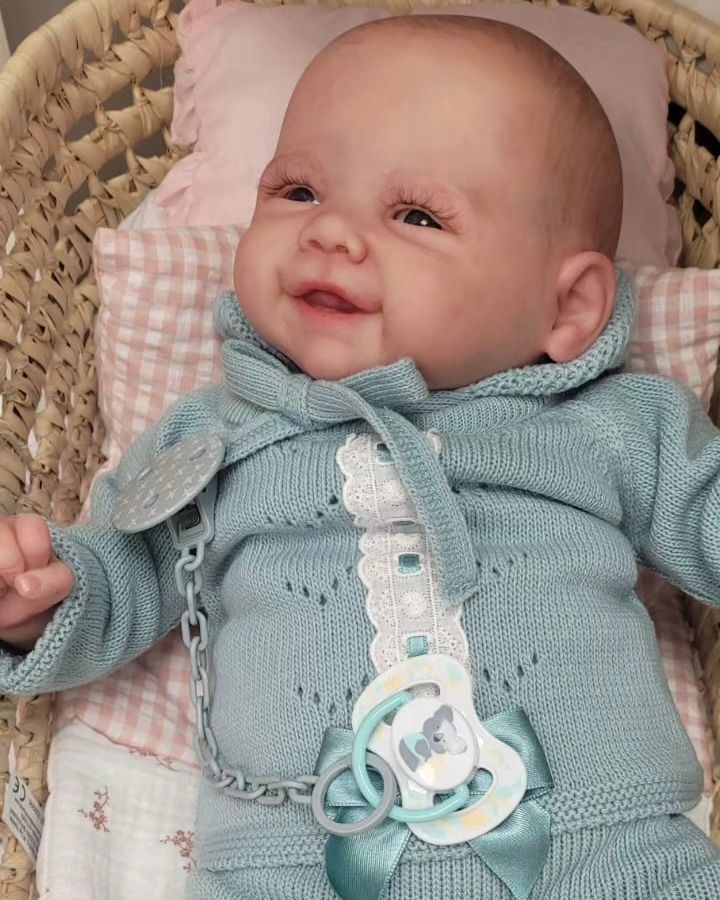 Bebé sonriente con un conjunto de punto azul acostado sobre una almohada rosa en una cesta tejida