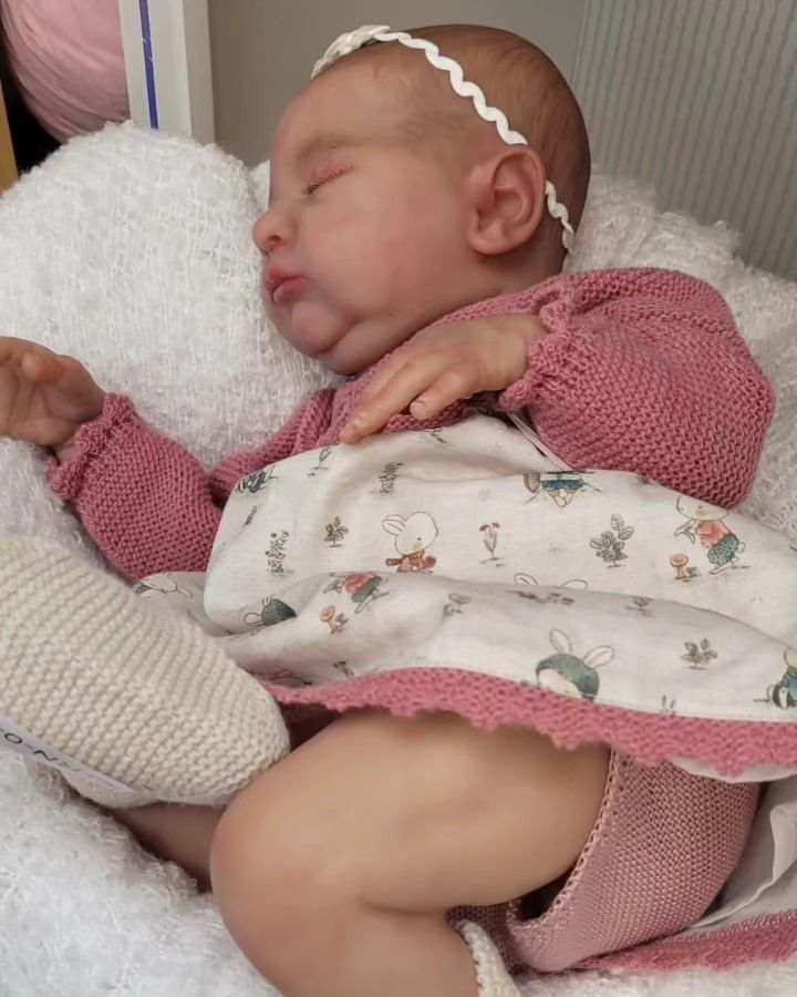 Un recién nacido duerme envuelto en una manta azul claro, sobre un cojín estampado.
