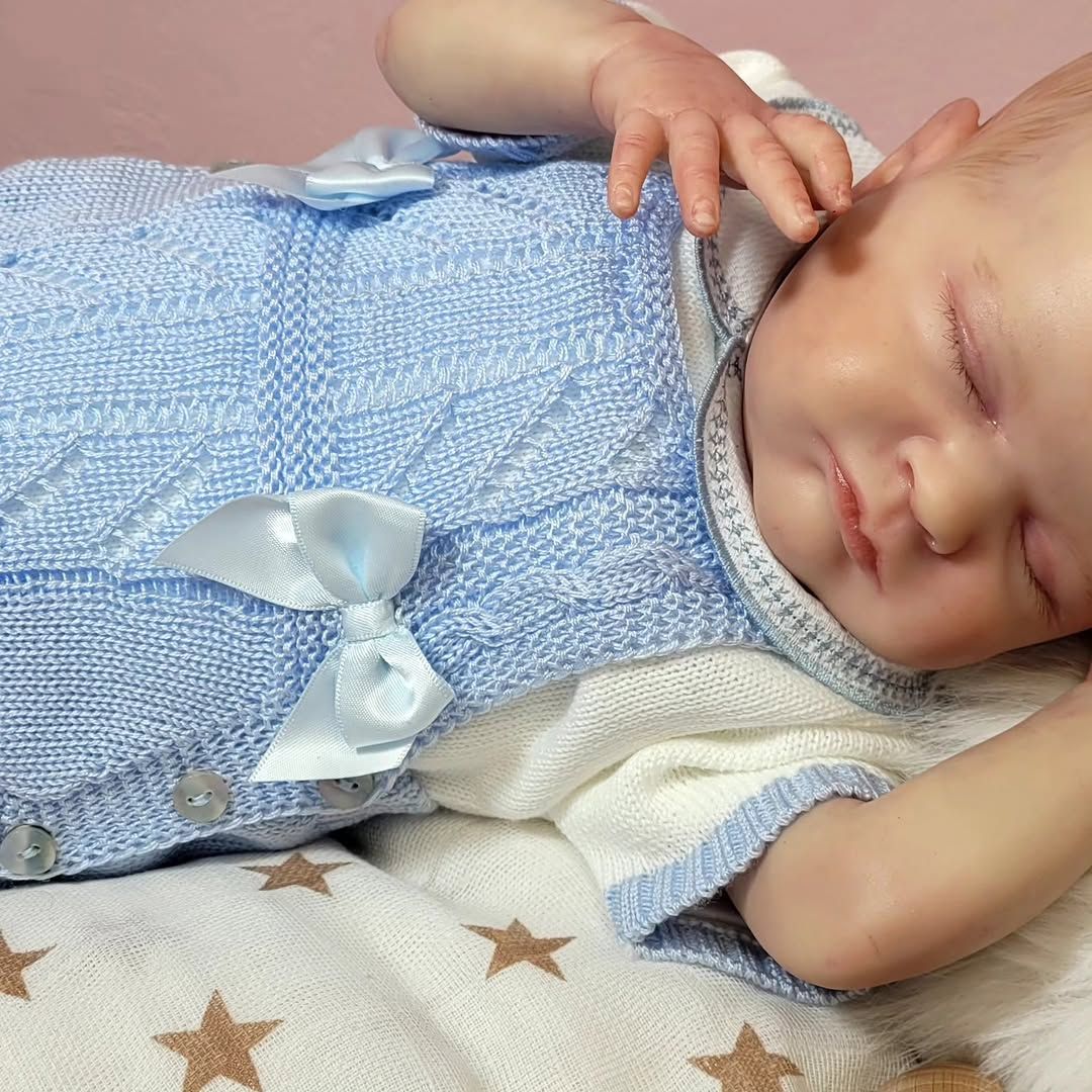 Bebé durmiendo con un conjunto de punto azul, descansando sobre una manta con estampado de estrellas.