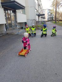 Neonliivit yllään olevat lapset ajavat skoottereilla koulurakennuksen ulkopuolella