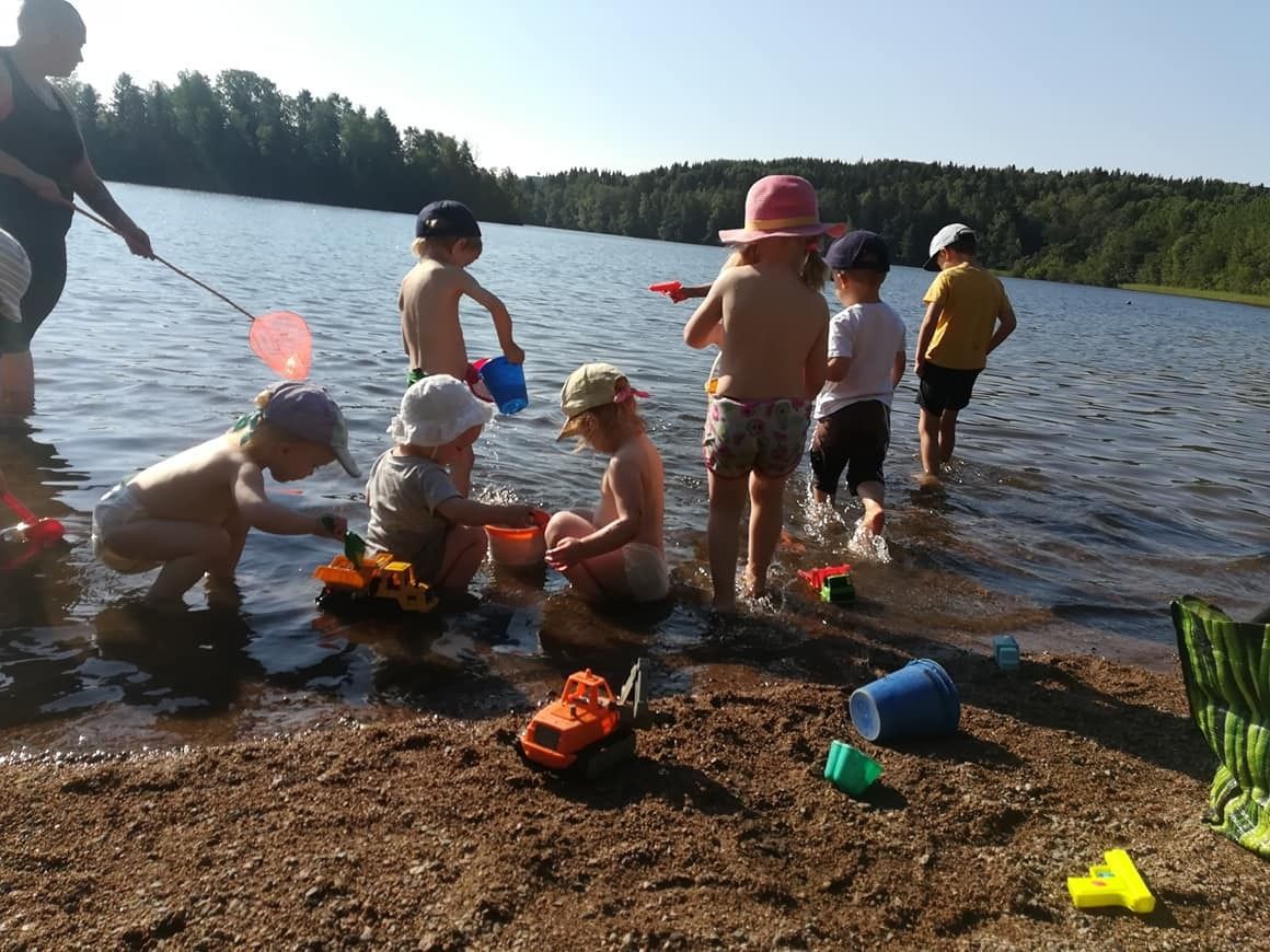 Lapset leikkivät ämpäreillä ja leluilla järven rannalla aurinkoisena päivänä