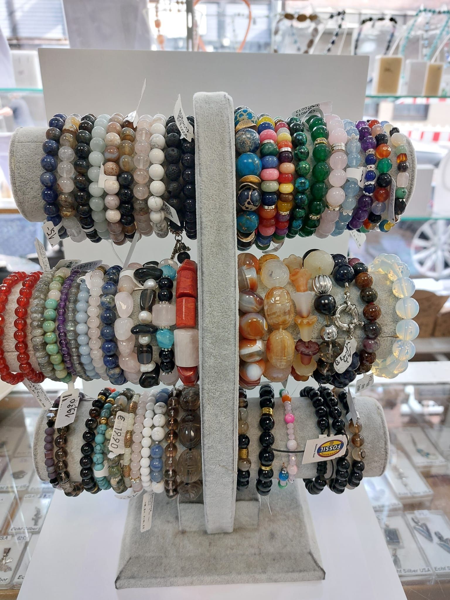 Ein drehbarer Schmuckständer, auf dem in einem Ladenlokal Reihen von mehrfarbigen Perlenarmbändern präsentiert werden.
