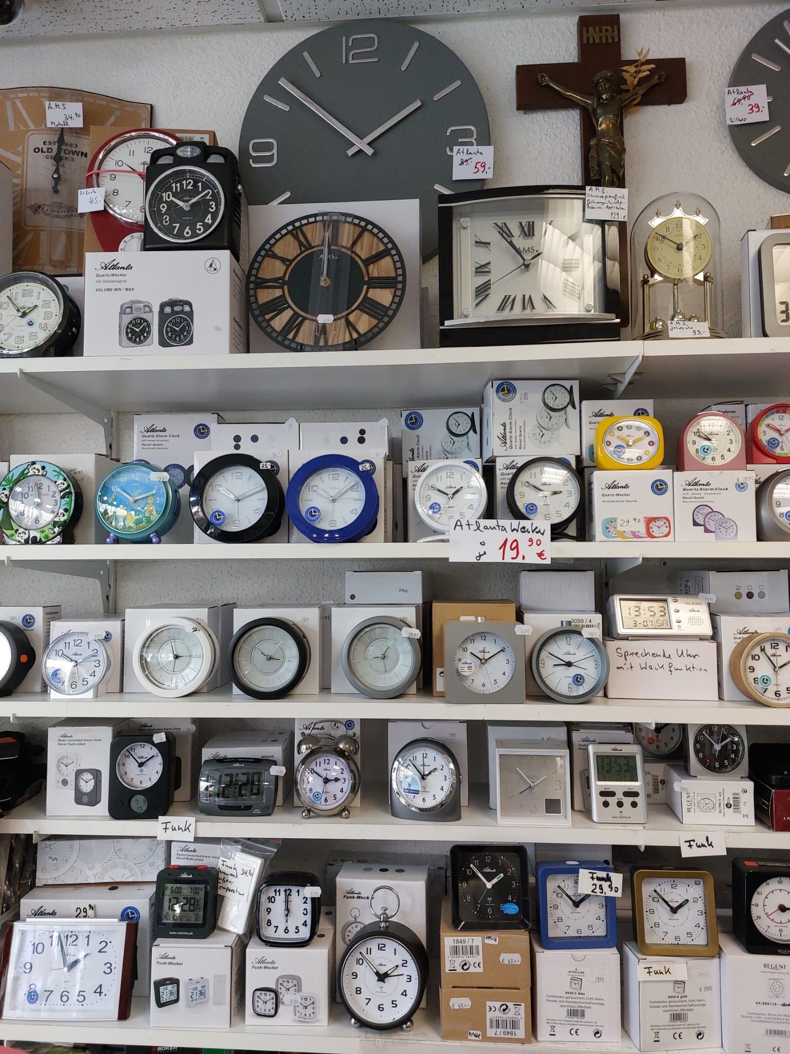 Regale voller verschiedener Uhren, darunter Wanduhren, Wecker und ein an der Wand befestigtes Kruzifix.
