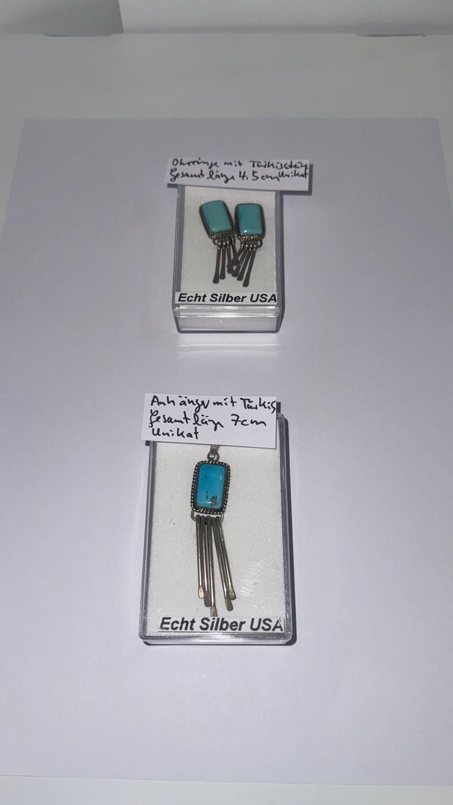 Zwei Süßwasserperlenketten, ein Paar Perlenohrringe in einer grünen Schachtel und handgeschriebene Preisschilder auf einer weißen Fläche.