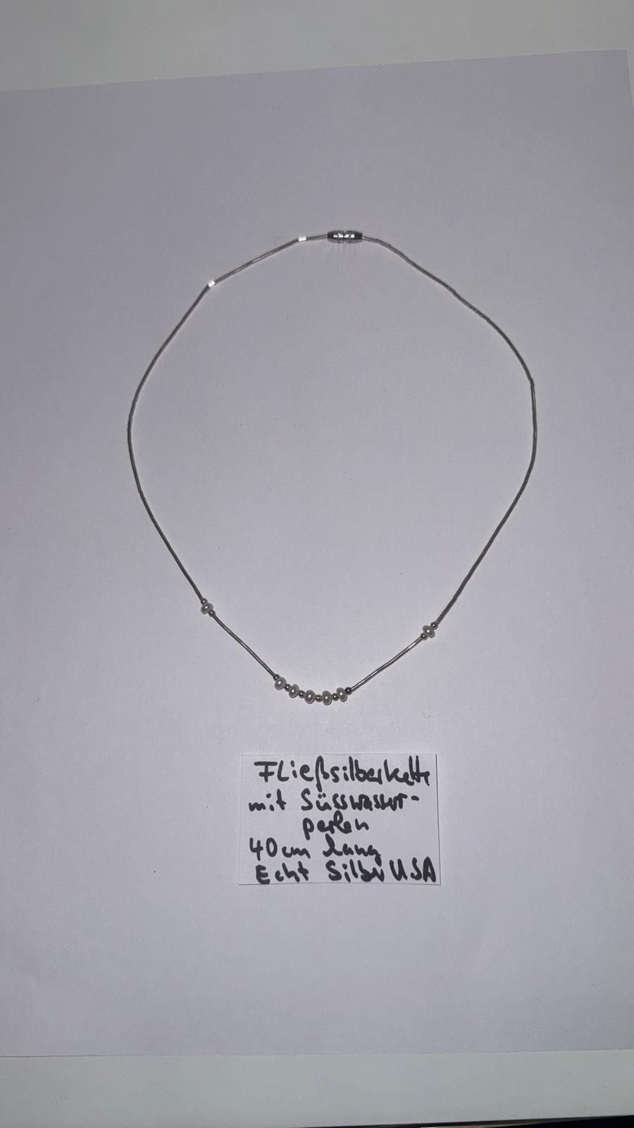 Halskette mit weißen Kristallen, Perlen und roten Perlen auf weißem Grund mit einem Hinweis zum Magnetverschluss.