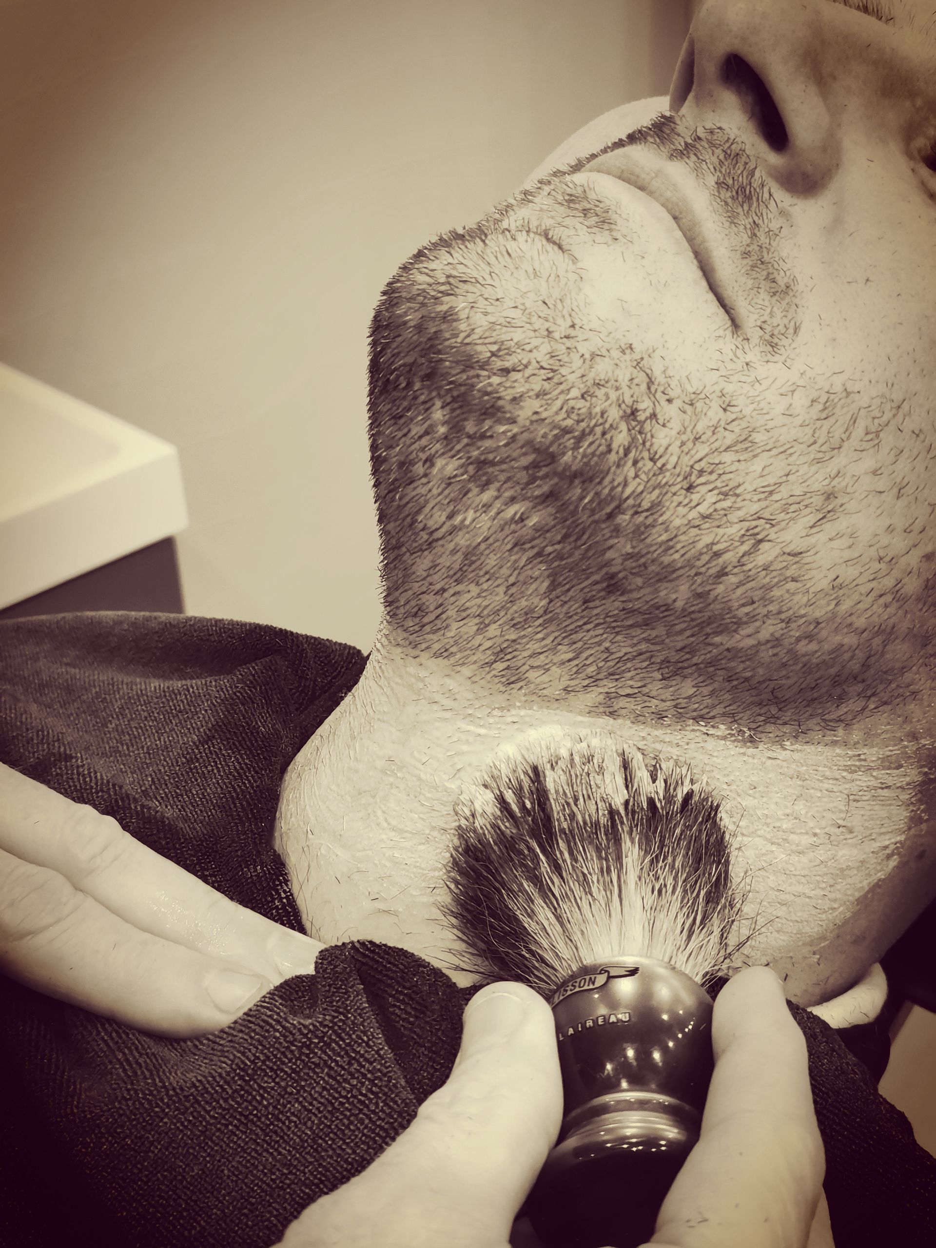 Un barbier utilise son blaireau pour appliquer la mousse à raser sur le cou d'un monsieur