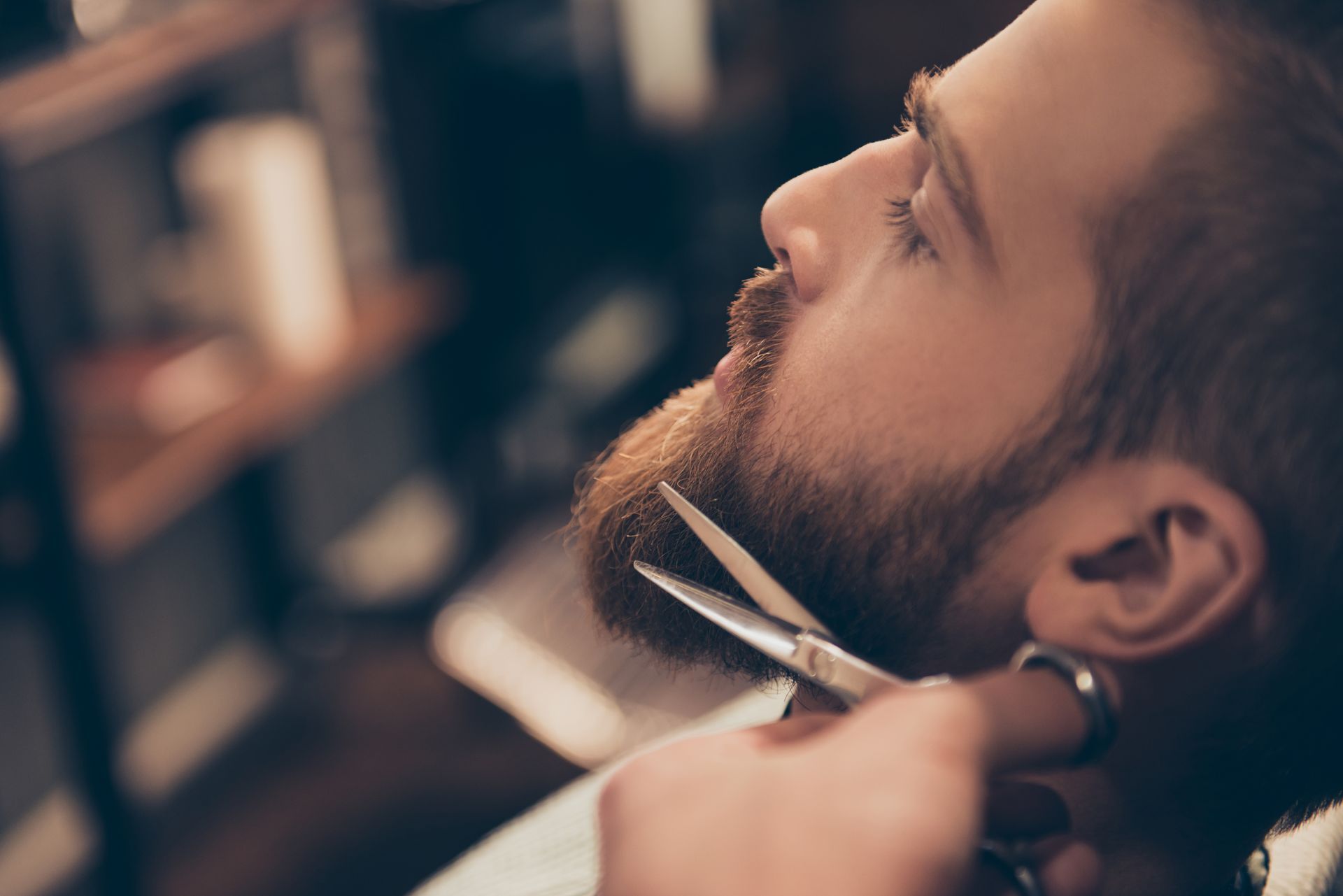 Un homme à la barbe rousse se fait tailler la barbe avec des ciseaux chez un coiffeur.
