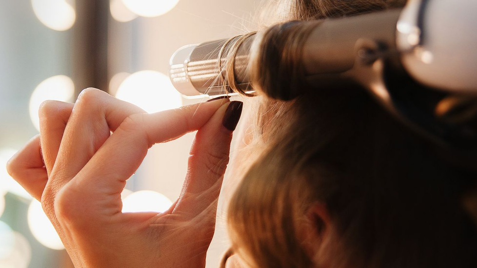 Femme bouclant ses cheveux avec un fer à friser, les mains en gros plan.
