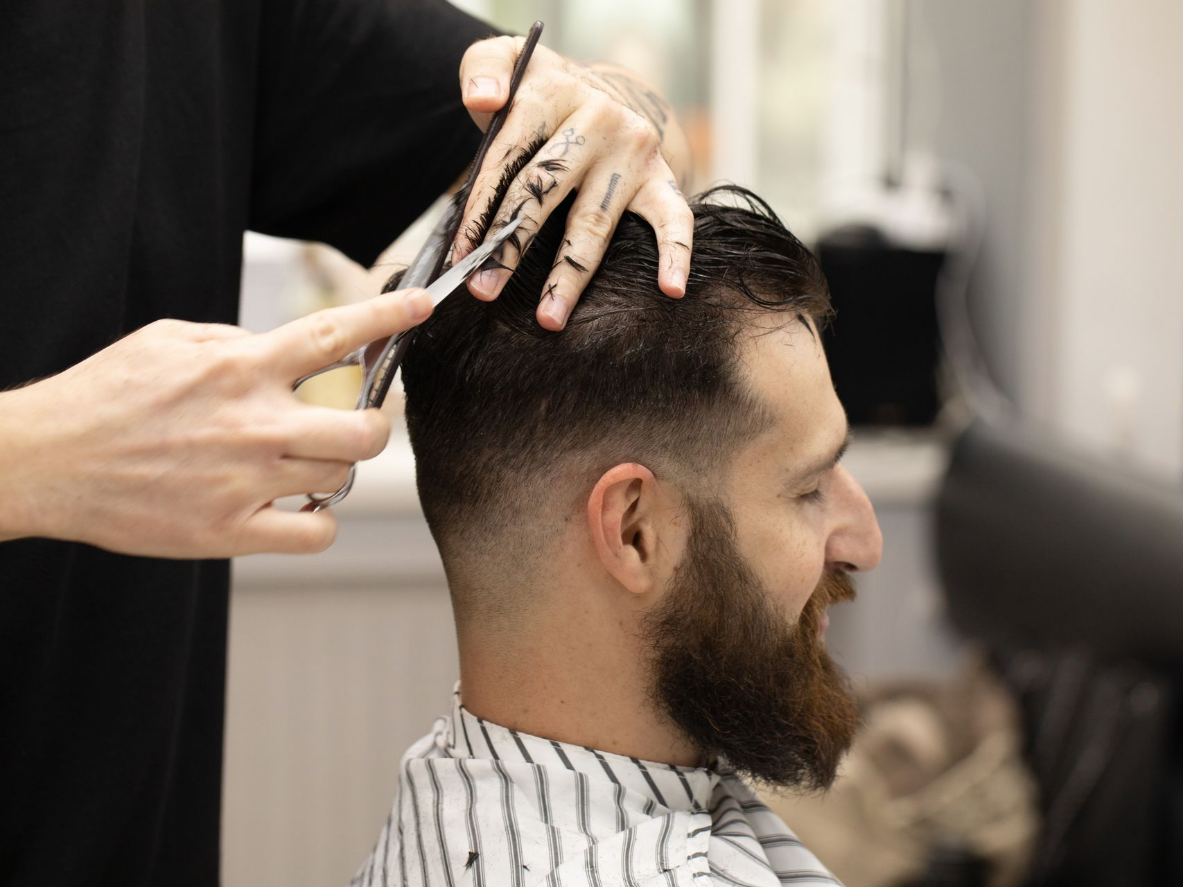 Un barbier coupe les cheveux d'un homme dans un salon de coiffure ; l'homme a une barbe et sourit.
