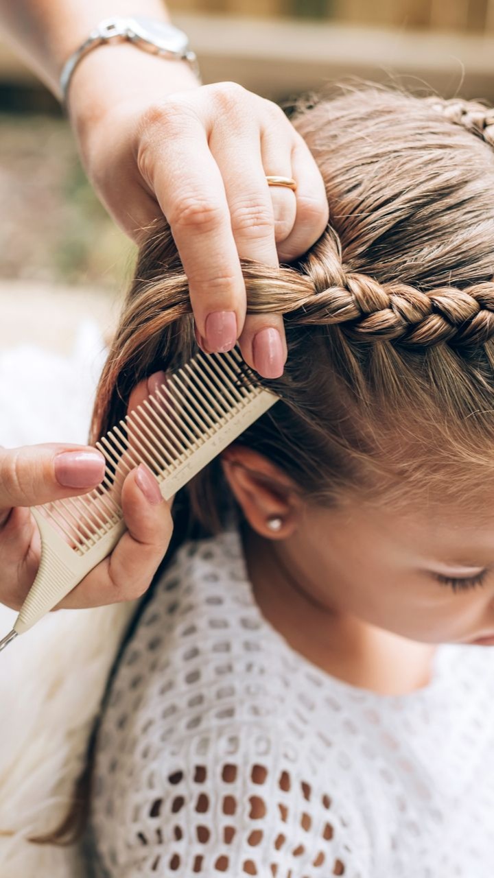 Mains d'une femme tressant les cheveux d'une fille à l'aide d'un peigne. Gros plan sur la couronne tressée en cours.