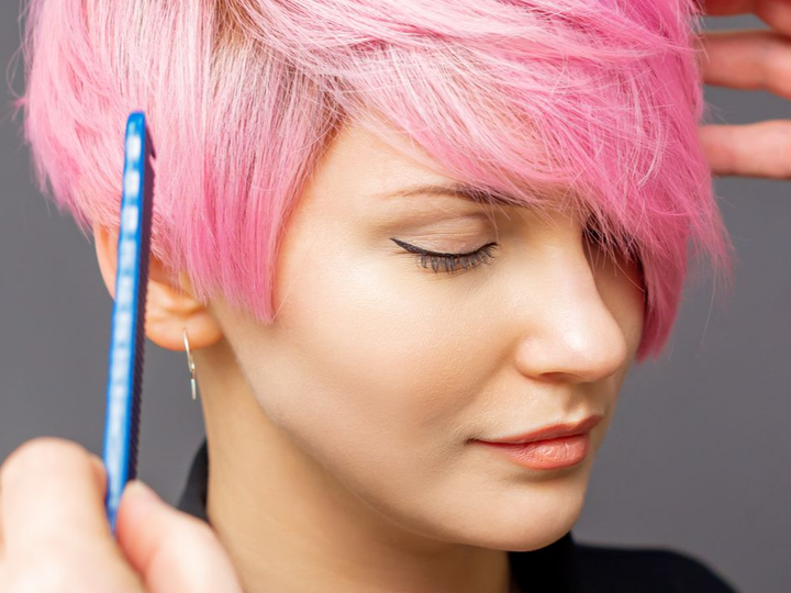 Femme aux cheveux roses courts coiffés avec un peigne bleu, les yeux fermés.