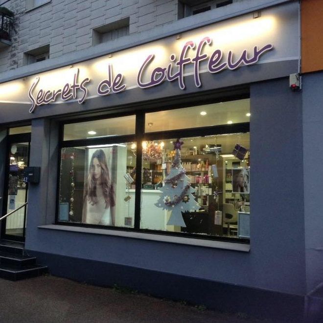 Une devanture avec Secrets de Coiffeur de noté. Elle présente l'intérieur d'un salon de coiffure et la photo d'une femme.