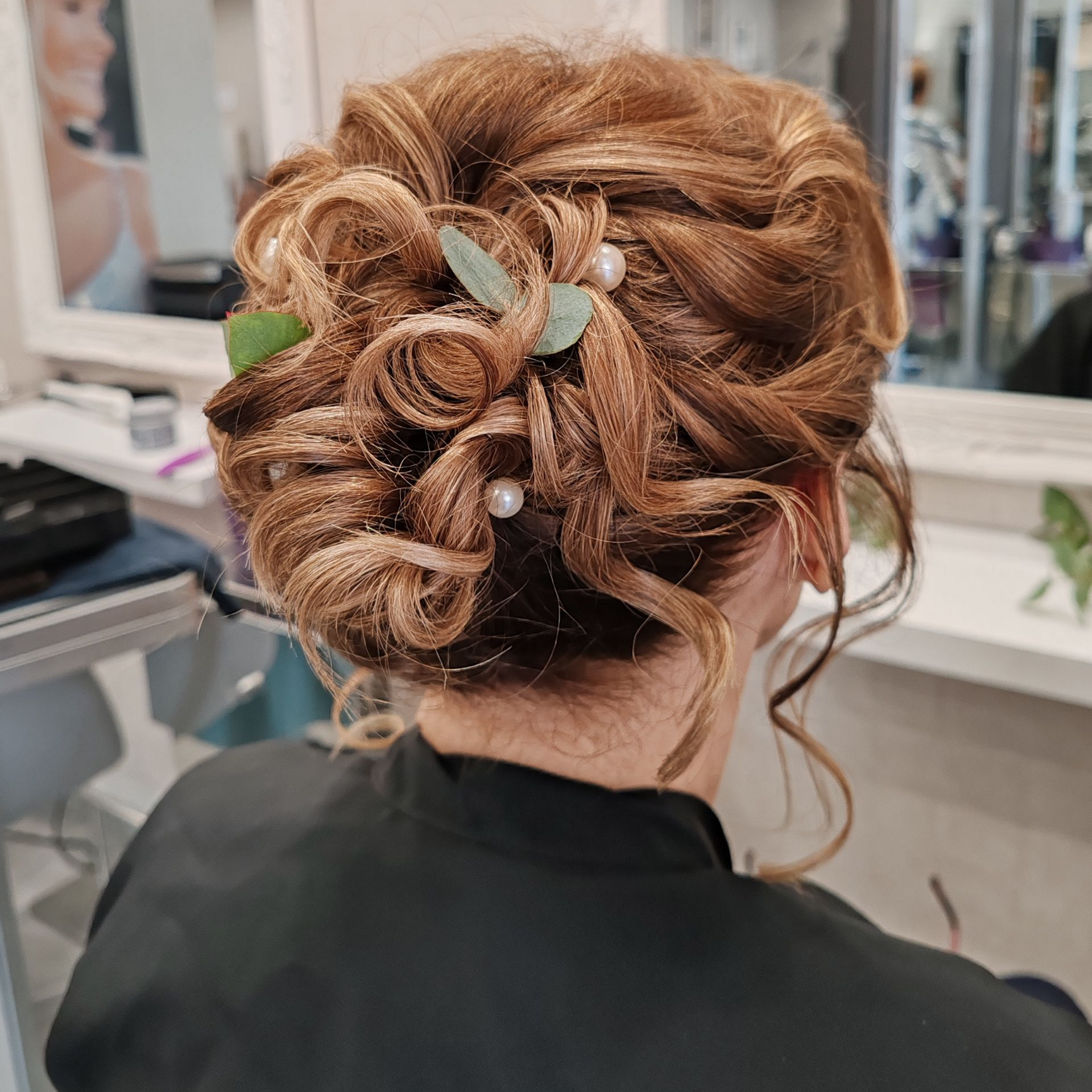 Femme avec une coiffure chignon bouclé avec des perles décoratives et de la verdure dans un salon.