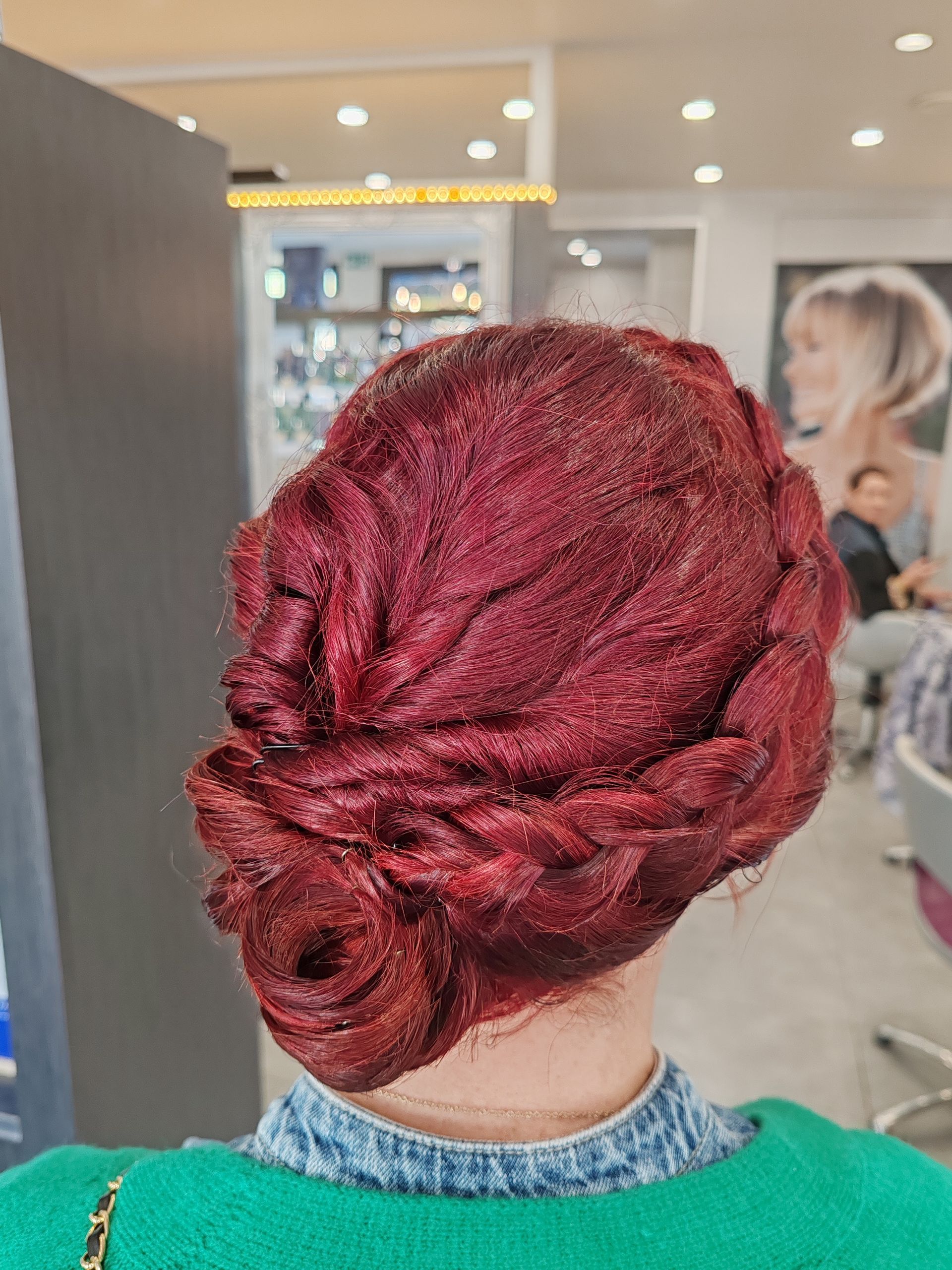 Femme avec une coiffure chignon rouge foncé dans un salon, vue de dos.