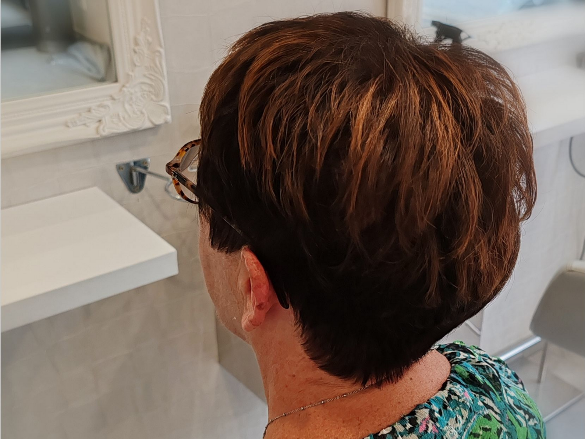 Femme aux cheveux courts, dégradés et auburn, portant des lunettes, assise dans un salon.