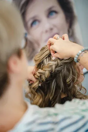 Femme avec un chignon tressé et des mèches bouclées, accessoirisé d'une pince à cheveux ; décor de salon.