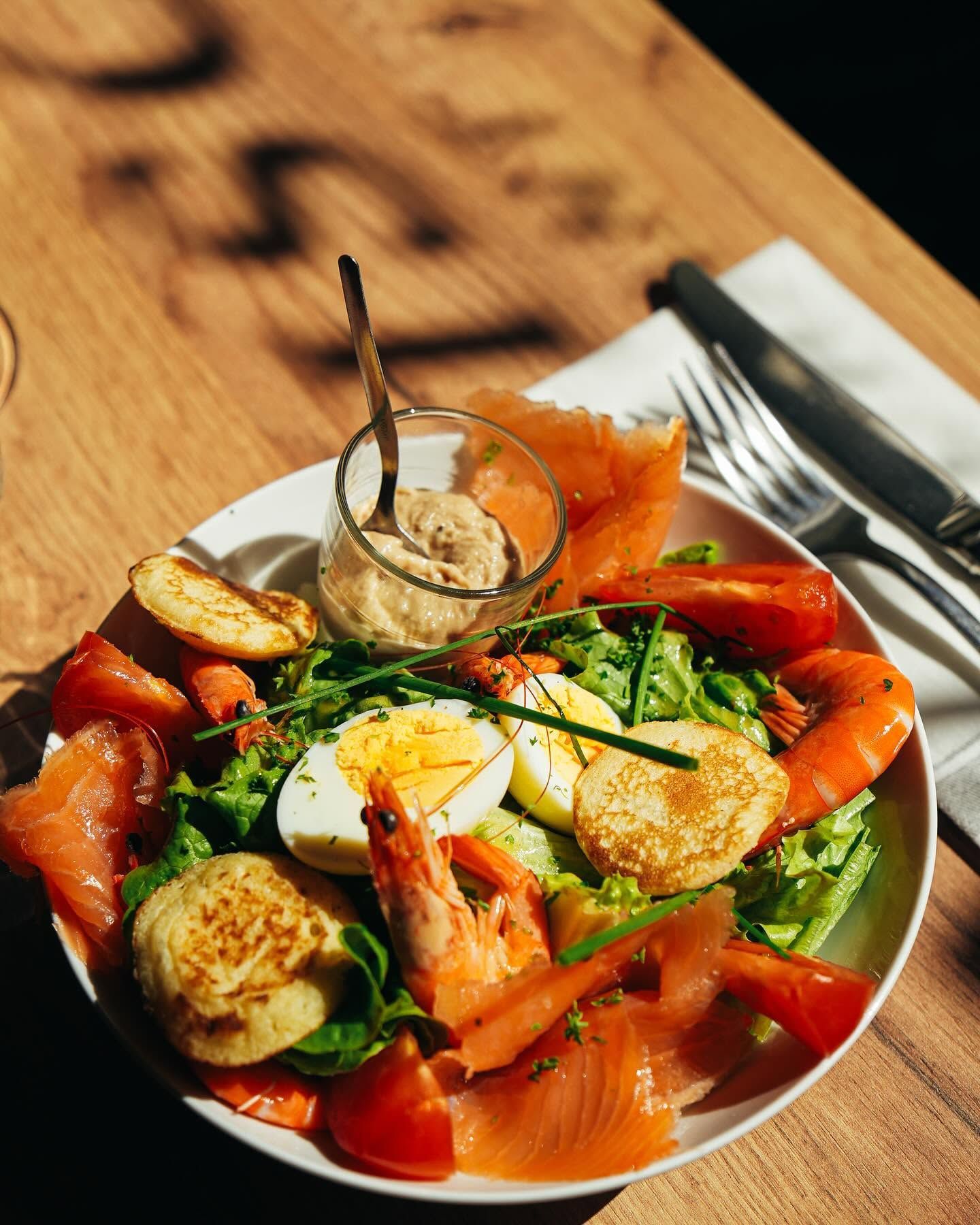 Une assiette avec des crevettes, du saumon, des œufs durs, de la salade verte et quelques blinis.