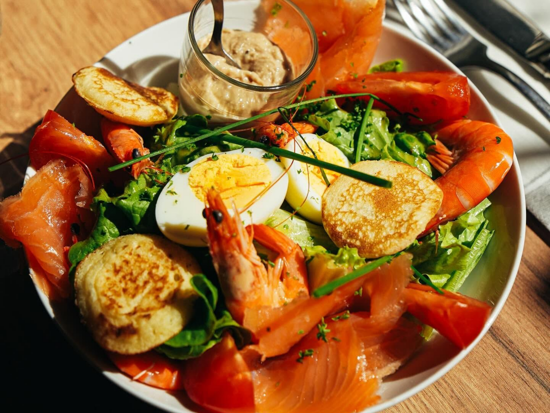 Une assiette avec des crevettes, du saumon, des œufs durs, quelques blinis et de la salade verte.