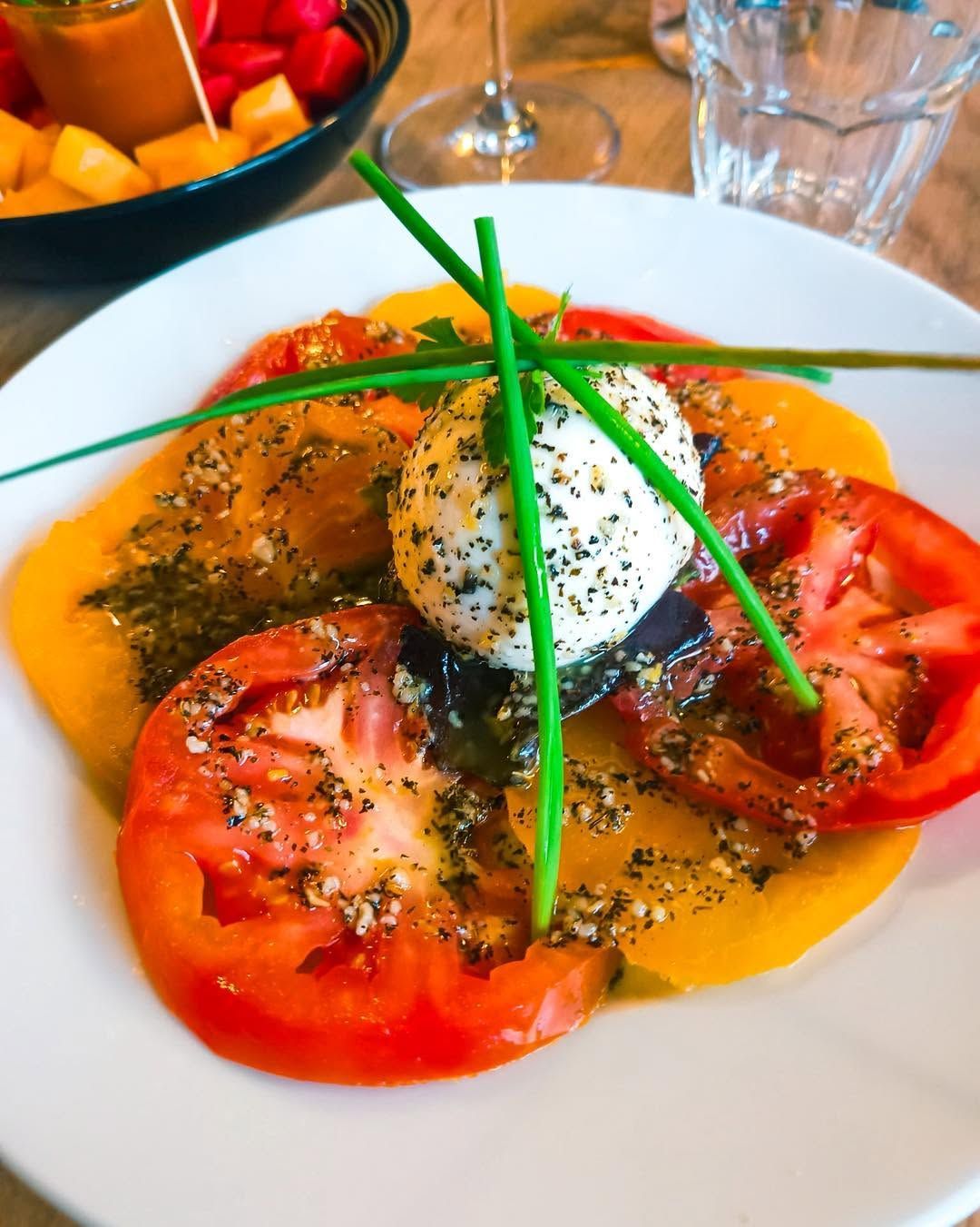 Des tranches de tomates avec une burrata au centre et des brins de ciboulette.