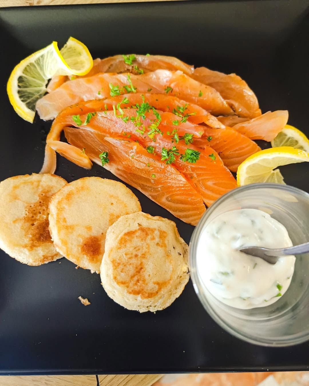 Des tranches de saumon fumé avec des blinis et une sauce à base de crème.