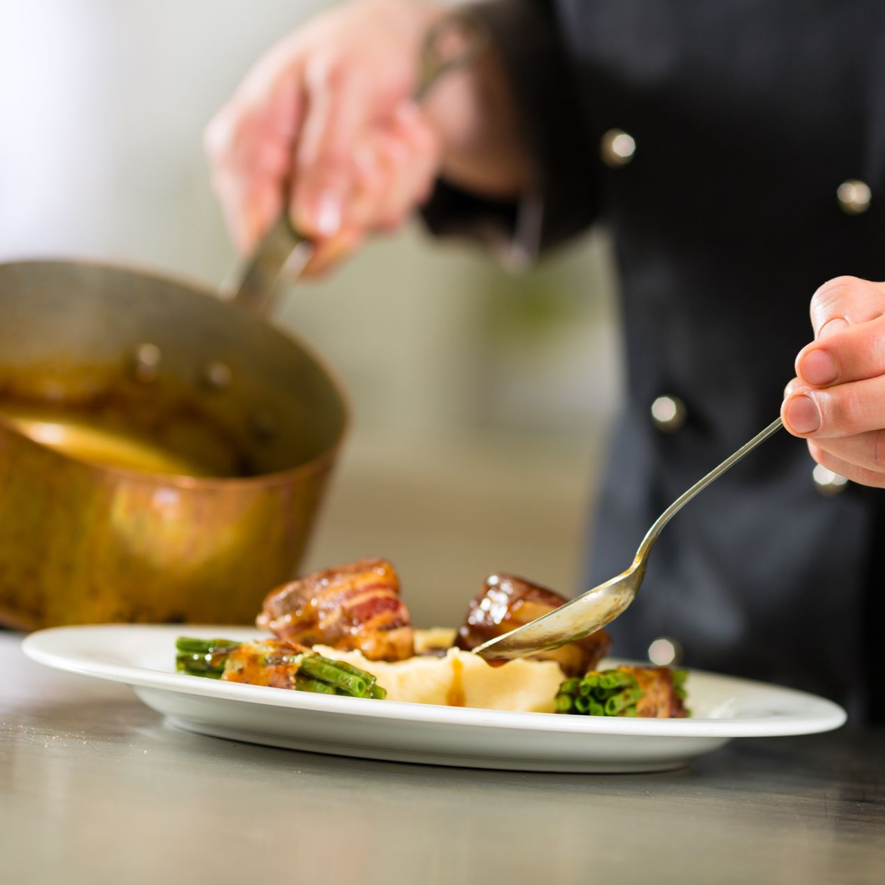 Un chef dresse un plat en ajoutant de la sauce à l’aide d’une cuillère.