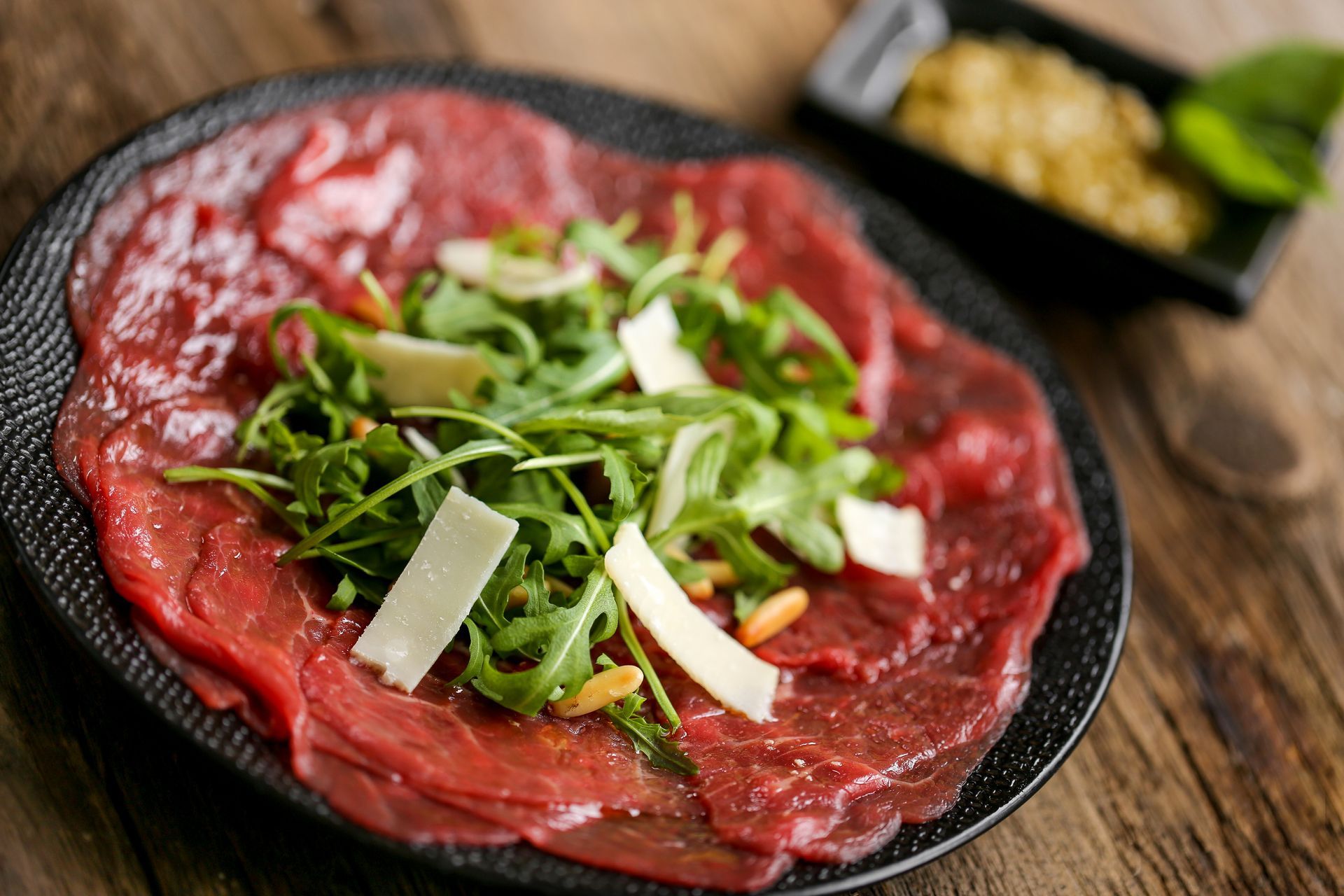 Une assiette de carpaccio de bœuf avec de la roquette au centre et quelques copeaux de parmesan.
