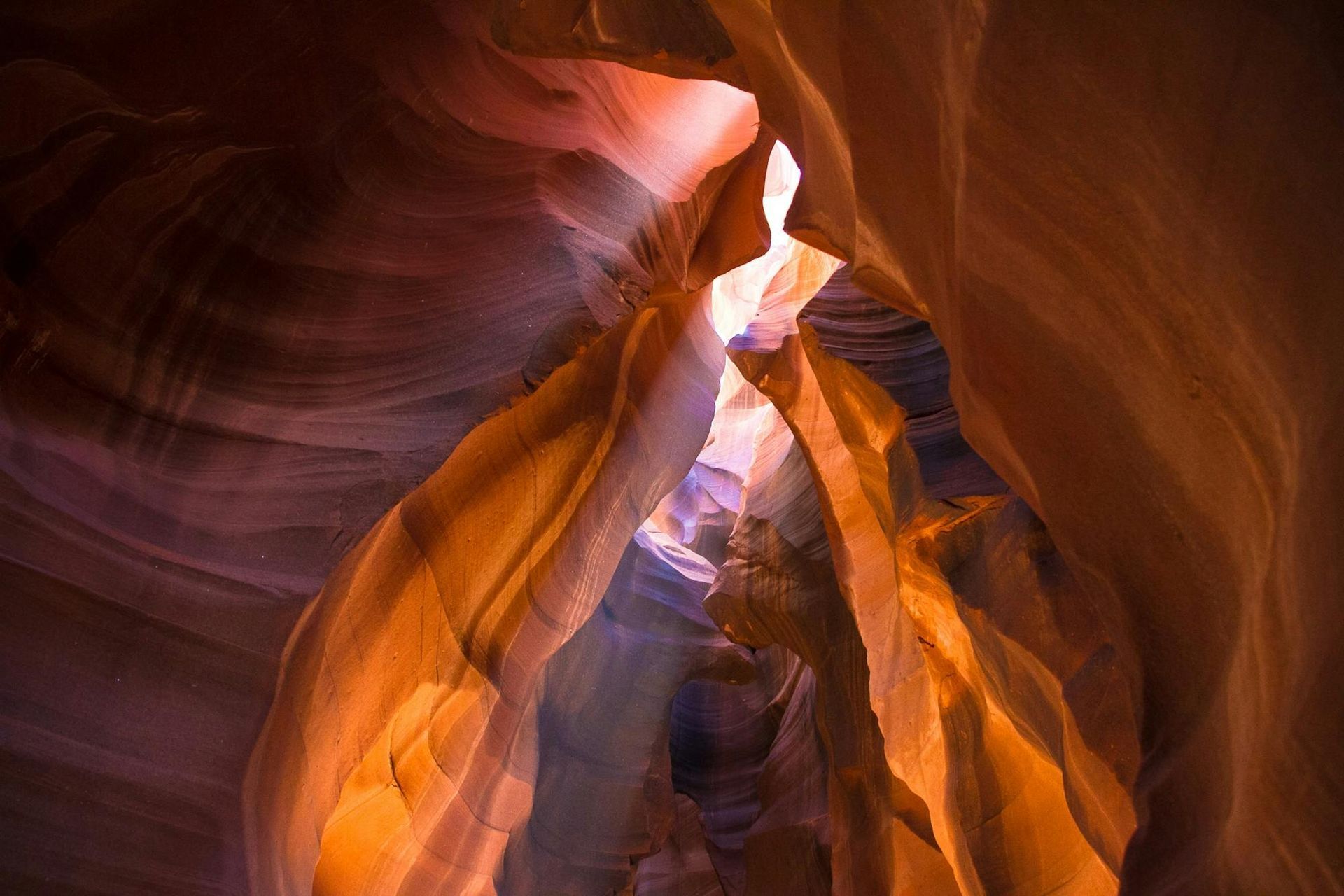 Sunlight illuminates sandstone canyon walls with swirling patterns.