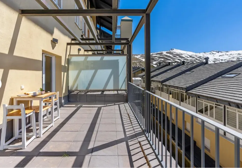 Terraza soleada en la azotea con mesas, sillas, barandillas y vistas a la montaña a través del parabrisas de cristal.