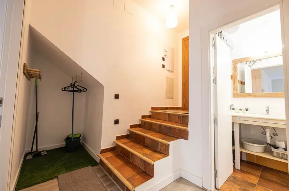 Entrada con escaleras de madera, perchero y un pequeño baño visible a través de una puerta abierta.