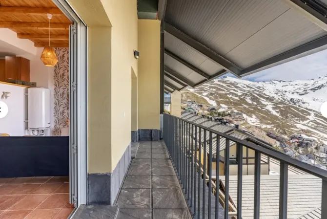 Pasillo con barandilla metálica en el balcón, con vistas a montañas nevadas, junto a una puerta abierta.
