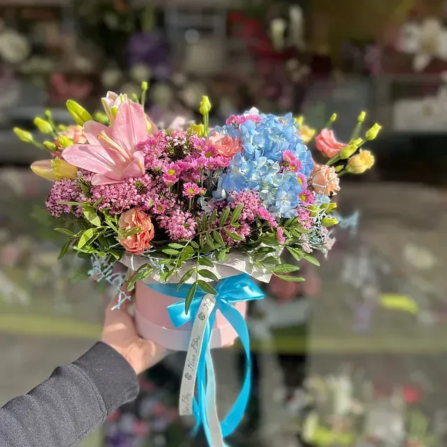 Una persona sostiene un jarrón de flores con una cinta azul.