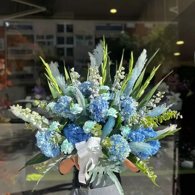 Una persona sostiene un jarrón con flores azules y blancas.