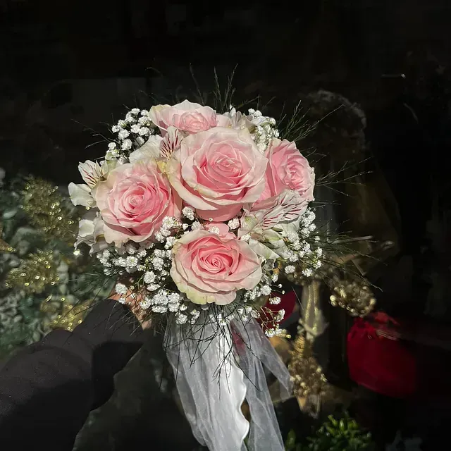 Una persona sostiene un ramo de rosas rosadas y aliento de bebé.