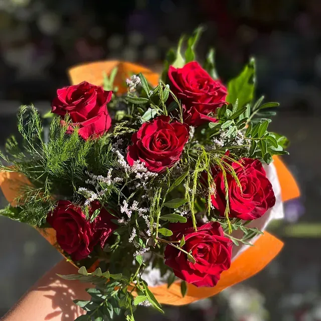 Una persona sostiene un ramo de rosas rojas y vegetación.