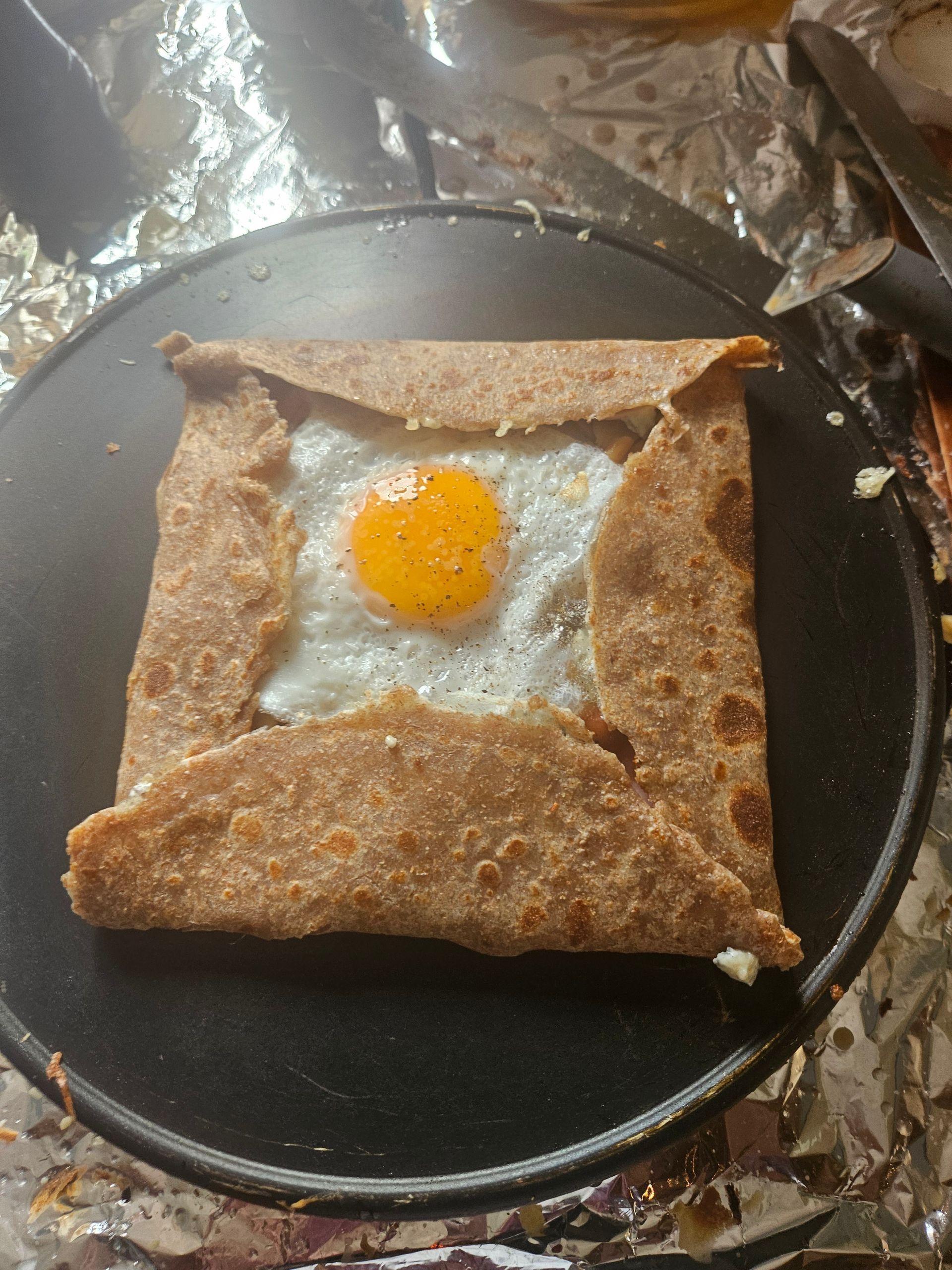 Crêpe salée avec un œuf au plat au centre, plié en forme de carré, sur une plaque chauffante chaude.