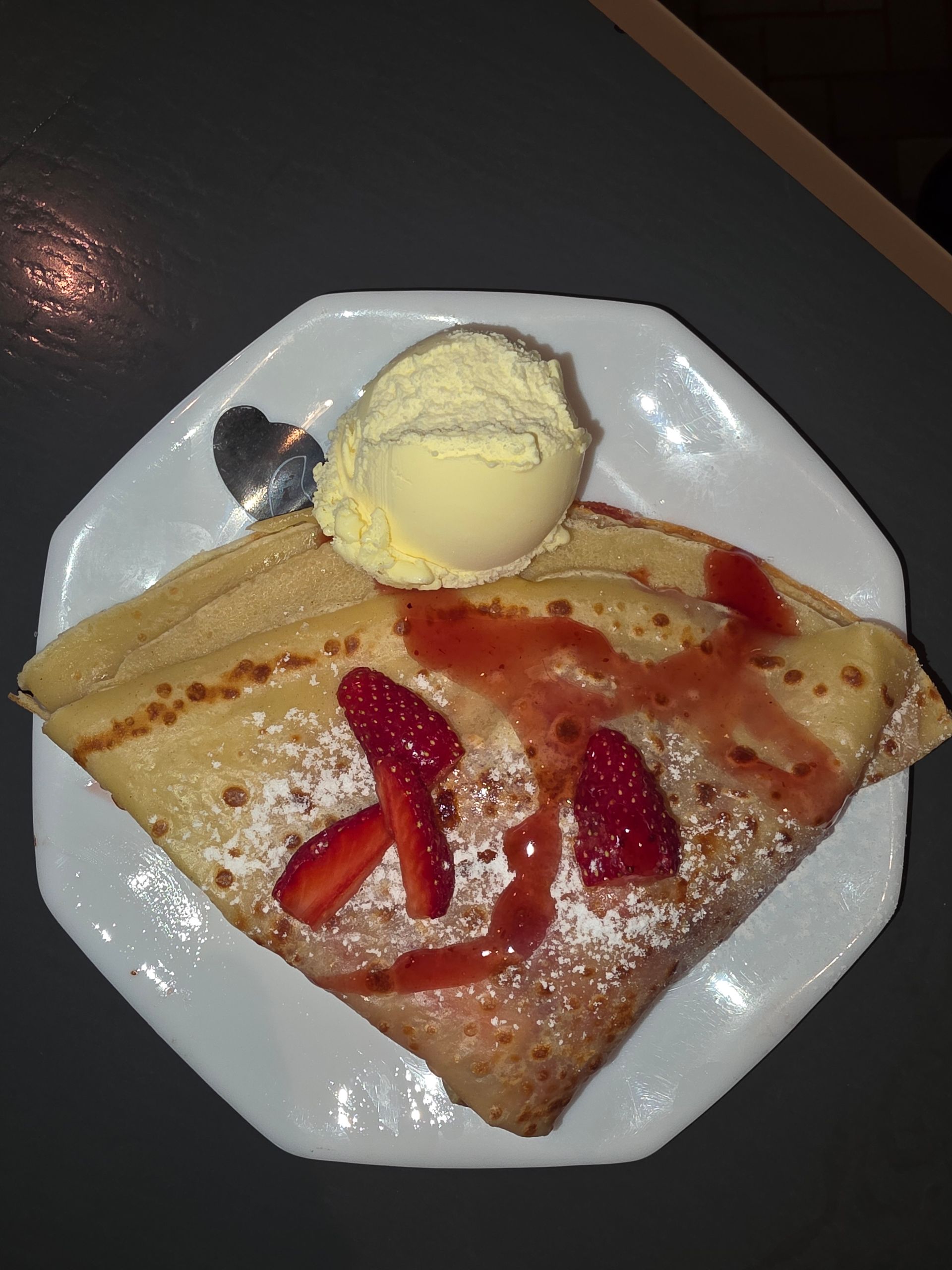 Crêpe aux fraises, sauce aux fraises et glace à la vanille sur une assiette blanche; saupoudrée de sucre glace.