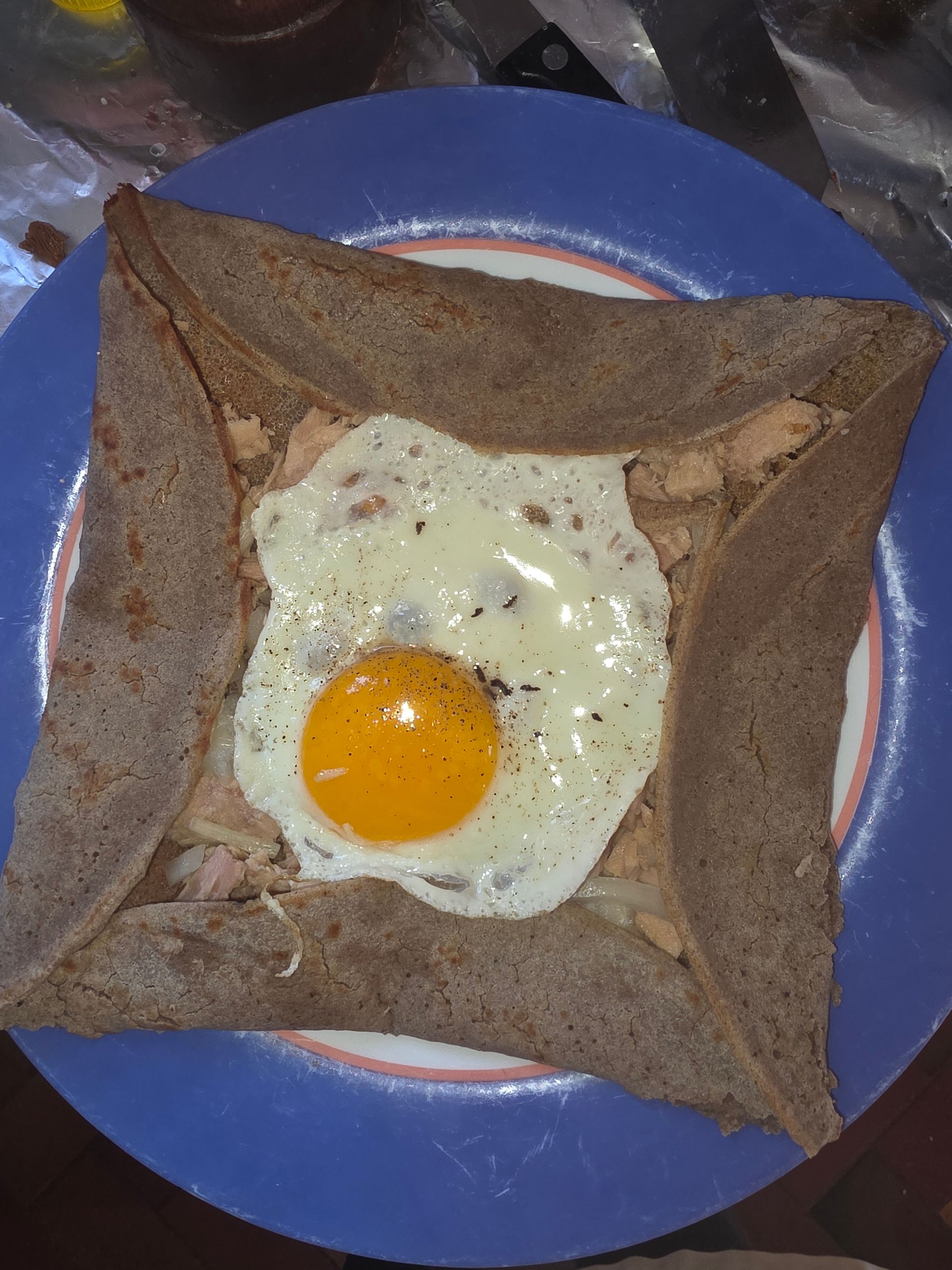 Crêpe de sarrasin salée sur une assiette bleue, pliée pour encadrer un œuf au plat avec un jaune orange vif.
