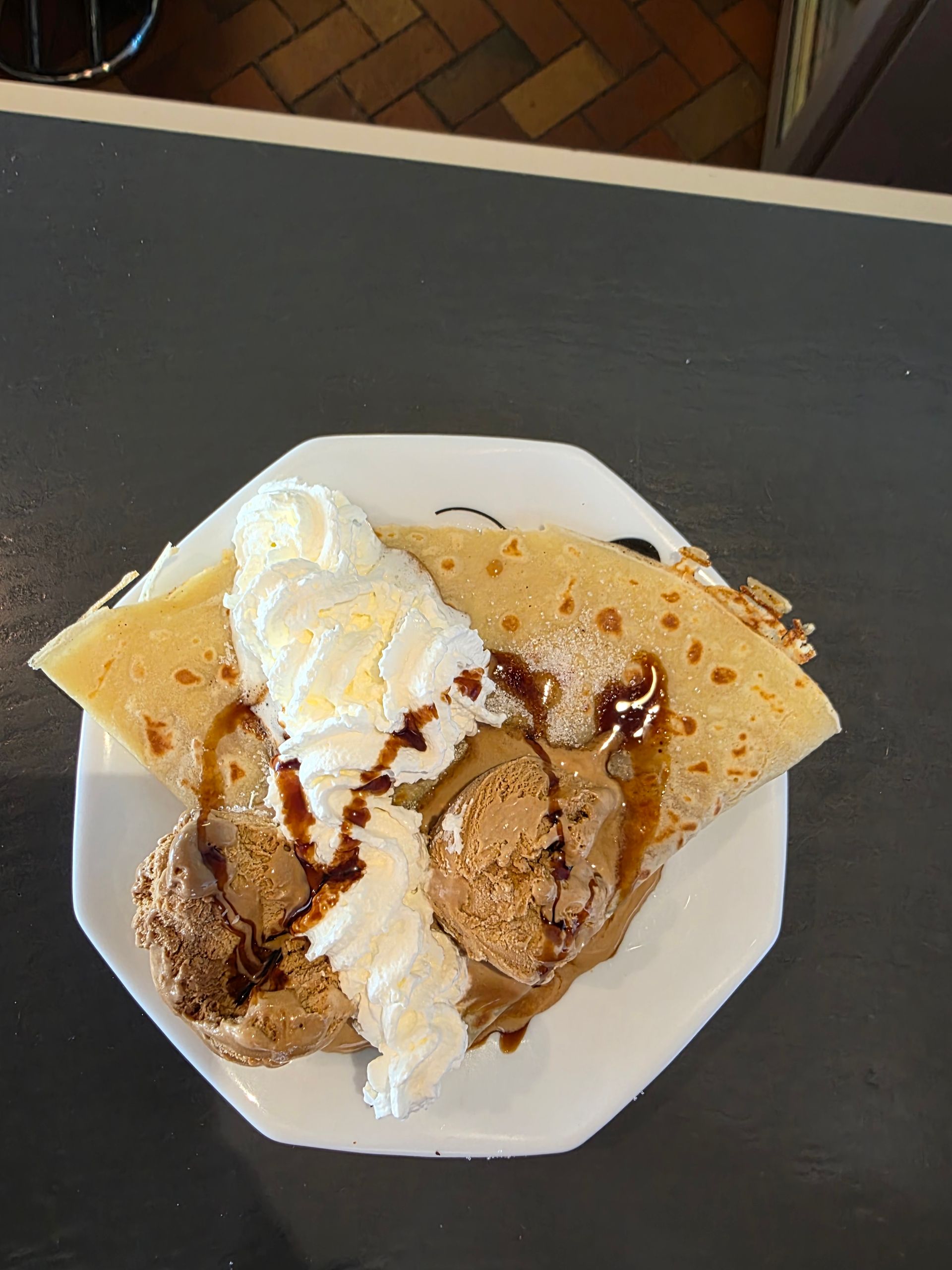 Crêpe avec glace au chocolat, crème fouettée et sirop de chocolat sur une assiette octogonale blanche.