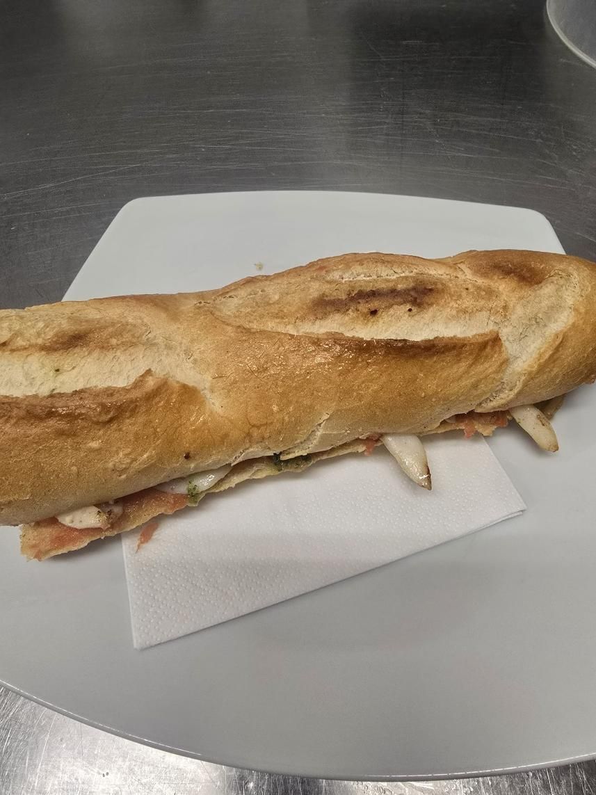 Un bocadillo de baguette tostada, de color marrón dorado, servido en un plato blanco con una servilleta.