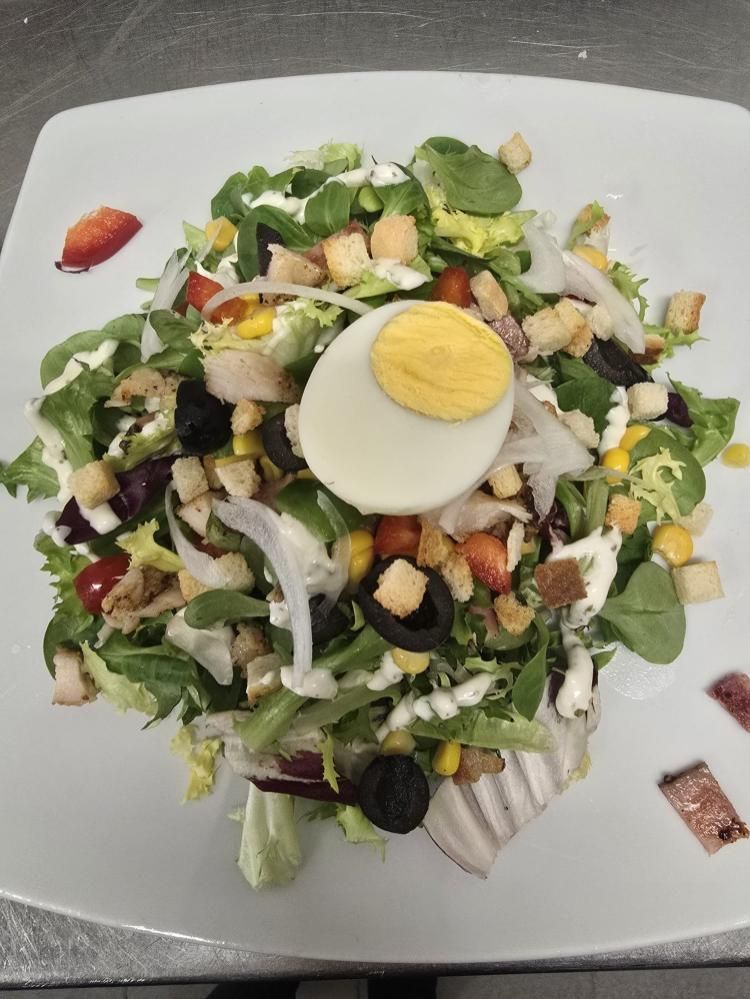 Una ensalada fresca, coronada con medio huevo duro, picatostes, maíz, cebolla en rodajas y aceitunas negras.