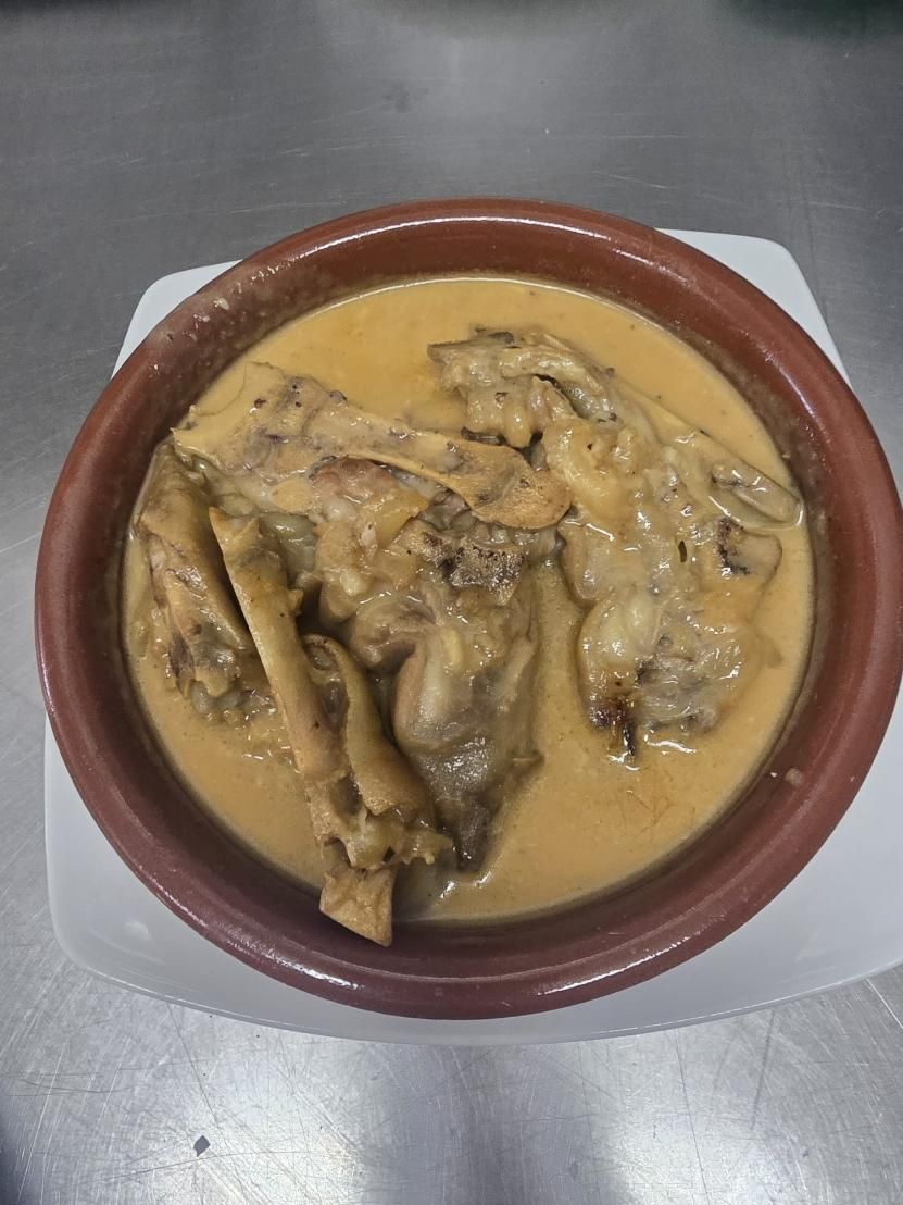 Un cuenco de barro lleno de trozos de conejo en una salsa espesa y cremosa de color marrón, que reposa sobre un plato blanco.