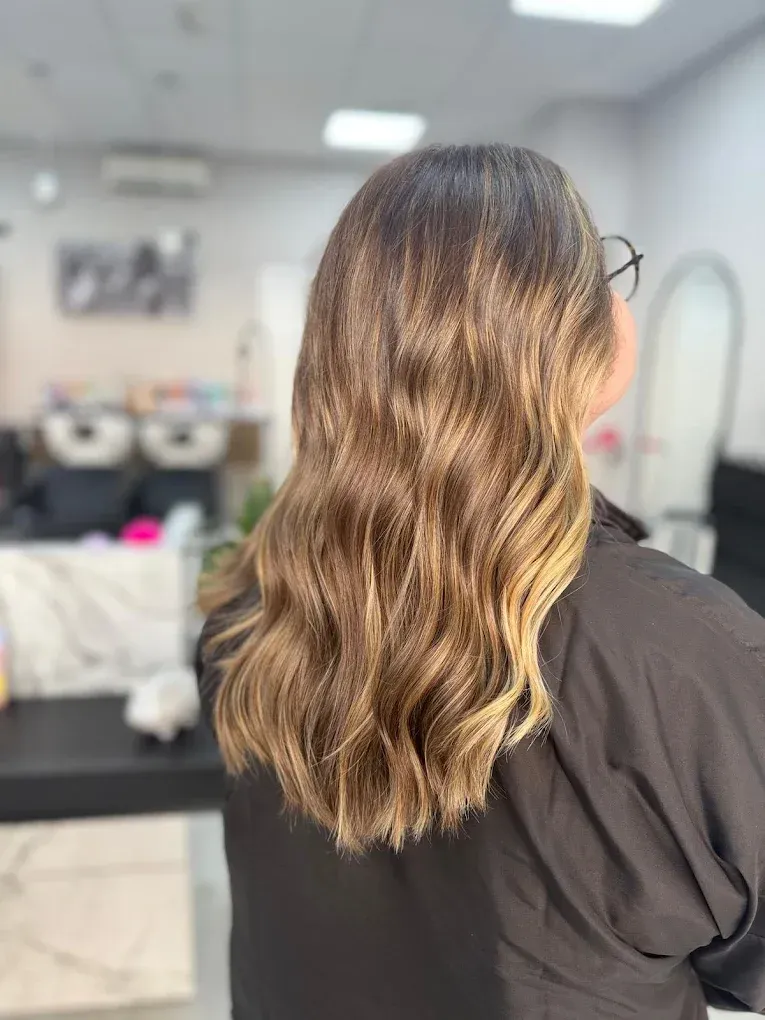 Mujer con cabello ondulado y con reflejos en un salón de belleza, vistiendo un top negro.