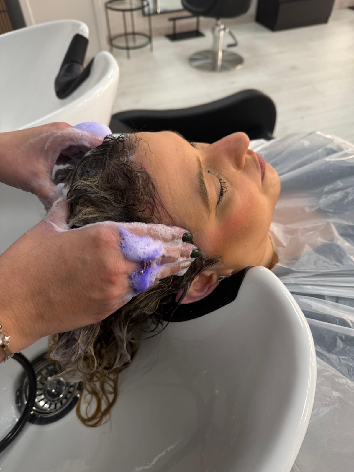 Mujer con cabello ondulado y con reflejos en un salón de belleza, vistiendo un top negro.