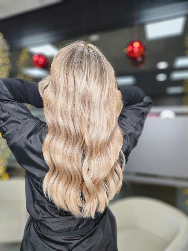 Mujer con cabello rizado, con efecto ombré desde las raíces oscuras hasta las puntas rubias, siendo peinada a mano.